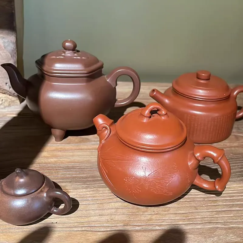 Clay teapots on a wooden shelf, beside a pink glazed jar and a painted lidded box